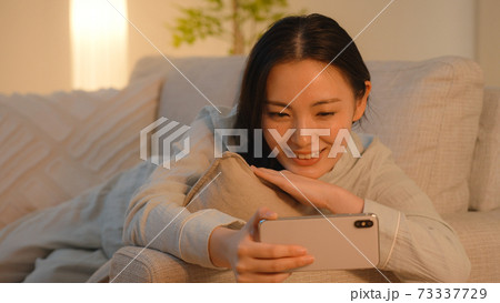 夜、ソファーでスマートフォンを見る若い女性 夜、ソファーでスマートフォンを見る若い女性 73337729