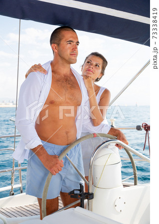 Couple standing at yacht wheel along coast of Barcelona Couple standing at yacht wheel along coast of Barcelona 73338419