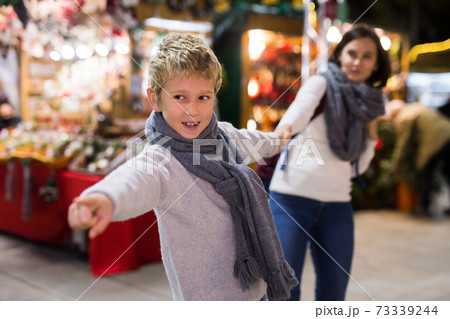 Preteen boy with mother reaching out for something at open air New Year fair 73339244