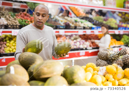 Middle aged man picking ripe melon at supermarket 73340526