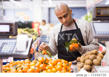 Spanish employee in fruits store with ripe tangerines Spanish employee in fruits store with ripe tangerines 73340726