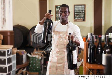 afro male seller of wine shop offering wine bottle to buy afro male seller of wine shop offering wine bottle to buy 73341428