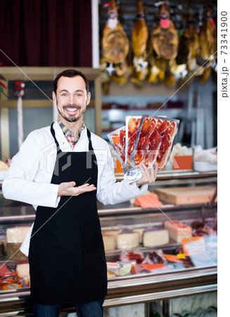 attractive man seller showing sliced bacon in shop 73341900