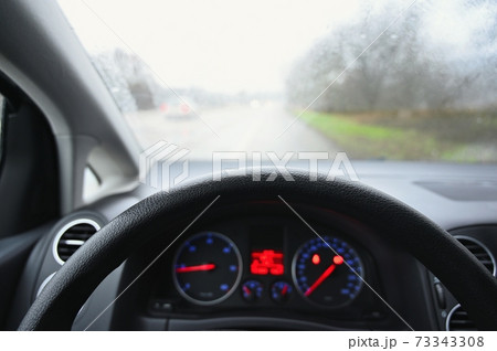 View from the driver - car interior with steering wheel and dashboard. Winter bad rainy weather and dangerous driving on the road. View from the driver - car interior with steering wheel and dashboard. Winter bad rainy weather and dangerous driving on the road. 73343308