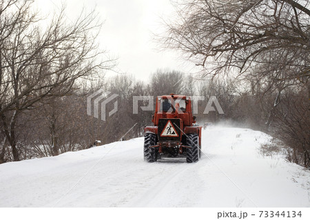 Old tractor clears the snow-covered road from snow blockages 73344134