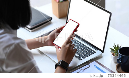 Close up view of businesswoman sitting at her workspace and using mock up mobile phone with blank screen. Close up view of businesswoman sitting at her workspace and using mock up mobile phone with blank screen. 73344466