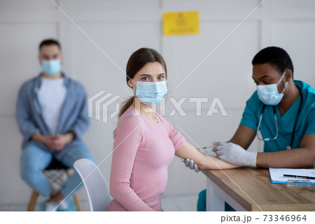 Black male doctor giving intramuscular injection to young woman at medical office Black male doctor giving intramuscular injection to young woman at medical office 73346964