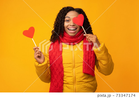 Black Woman Posing With Paper Hearts Covering Eye, Yellow Background 73347174