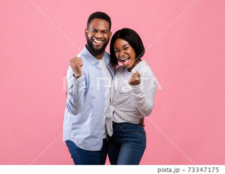 Positive black couple making YES gesture, feeling triumphant, celebrating their success on pink studio background 73347175