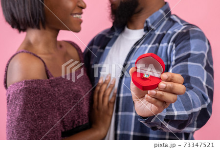 Cropped view of black couple holding box with engagement ring on pink studio background, panorama Cropped view of black couple holding box with engagement ring on pink studio background, panorama 73347521