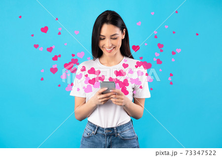 Woman sending love text message on cellphone, hearts flying away Woman sending love text message on cellphone, hearts flying away 73347522