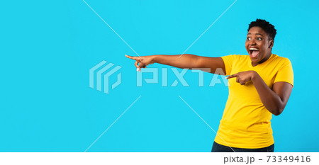 Excited Overweight African Lady Pointing Fingers Aside Over Blue Background Excited Overweight African Lady Pointing Fingers Aside Over Blue Background 73349416