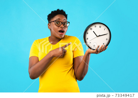 Oversized African Woman Showing Clock Posing Standing Over Blue Background Oversized African Woman Showing Clock Posing Standing Over Blue Background 73349417