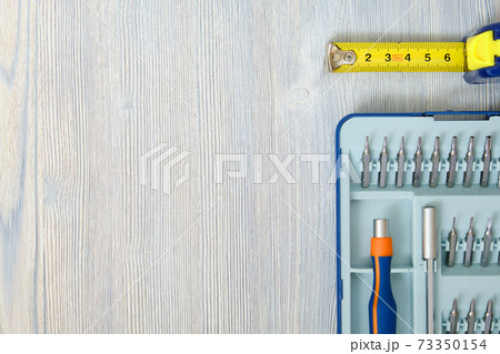 Screwdriver with interchangeable nozzles and tape measure with meter on a wooden gray background with copy space, top view. Screwdriver with interchangeable nozzles and tape measure with meter on a wooden gray background with copy space, top view. 73350154