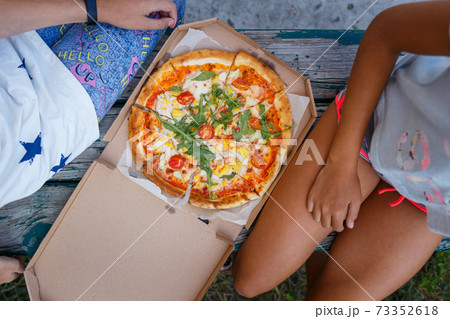 Two teenage girls sitting outdoor with pizza 73352618