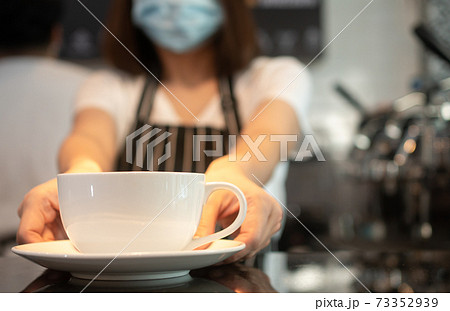 Asian waitress woman wearing face masks To prevent contagious diseases And is holding coffee cups to serve customers in the coffee shop. The concept of safety and prevention from COVID 19 outbreak Asian waitress woman wearing face masks To prevent contagious diseases And is holding coffee cups to serve customers in the coffee shop. The concept of safety and prevention from COVID 19 outbreak 73352939