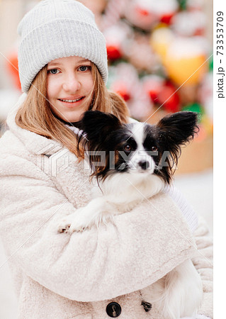 Beautiful girl with dog Papillon in her arms on winter Christmas streets 73353709