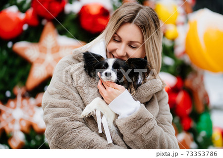 beautiful woman with dog Papillon near the Christmas tree on the street. 73353786