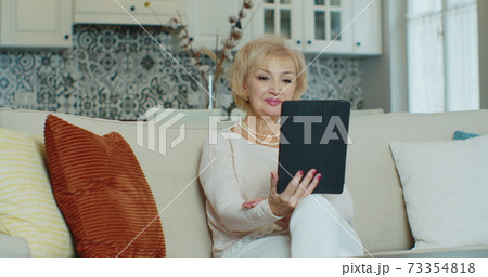 Happy senior old couple laughing talking relaxing on sofa using digital tablet, cheerful mature aged family spending time with gadget having fun. 73354818