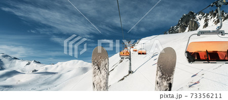 Scenic panoramic view of alpine peaks with ski lift ropeway on hilghland mountain winter resort and snow making machines on bright cold sunny day. downhill slopes with people and clear blue sky Scenic panoramic view of alpine peaks with ski lift ropeway on hilghland mountain winter resort and snow making machines on bright cold sunny day. downhill slopes with people and clear blue sky 73356211