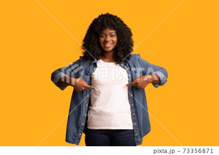 Attractive happy black lady pointing at her white blank t-shirt 73356871
