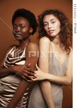 two pretty girls african and caucasian blond posing cheerful together on brown background, ethnicity diverse lifestyle people concept two pretty girls african and caucasian blond posing cheerful together on brown background, ethnicity diverse lifestyle people concept 73357115