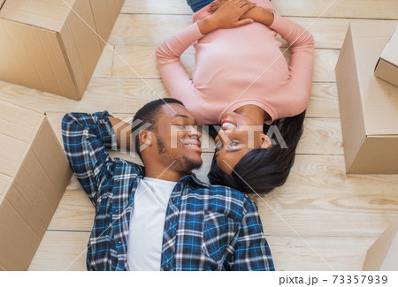 Above view of young black guy and his girlfriend lying on floor among carton boxes, looking at each other on moving day Above view of young black guy and his girlfriend lying on floor among carton boxes, looking at each other on moving day 73357939