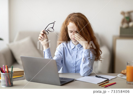 Tired red-haired schoolgirl rubbing her dry irritated eyes Tired red-haired schoolgirl rubbing her dry irritated eyes 73358406