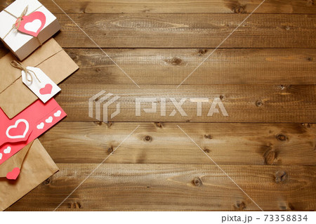Gifts and envelopes, colored and wrapped in brown craft paper, tied with twine with bows and labels, hearts on wooden planks background. Love, Valentine's, mother's, women's day, romantic template Gifts and envelopes, colored and wrapped in brown craft paper, tied with twine with bows and labels, hearts on wooden planks background. Love, Valentine's, mother's, women's day, romantic template 73358834