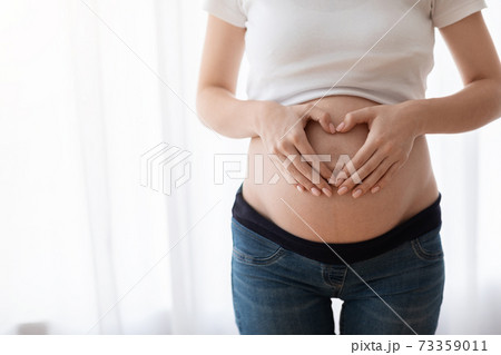 Unrecognizable pregnant woman holding hands in heart shape on her naked belly 73359011