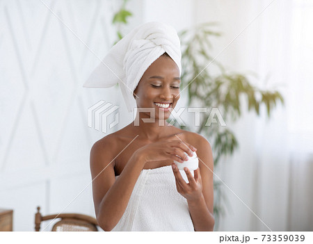 Cosmetics against wrinkles and skin problems. Young happy african american female blogger opens jar of cream Cosmetics against wrinkles and skin problems. Young happy african american female blogger opens jar of cream 73359039