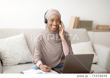 Muslim businesswoman in hijab taking notes during online meeting with colleagues on laptop at home office 73359040