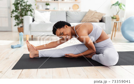 Flexibility exercises. Athletic young woman doing yoga on mat, stretching her legs during home workout Flexibility exercises. Athletic young woman doing yoga on mat, stretching her legs during home workout 73359041