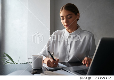 Woman writing in copybook and working on laptop Woman writing in copybook and working on laptop 73359312