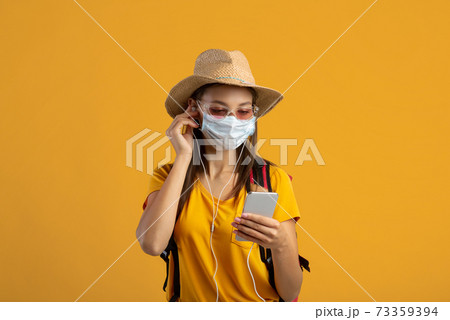 Female traveler in face mask listening to music on smartphone Female traveler in face mask listening to music on smartphone 73359394