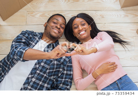 Loving black couple making heart with their hands, lying on floor surrounded by boxes on relocation day, top view Loving black couple making heart with their hands, lying on floor surrounded by boxes on relocation day, top view 73359434