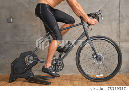 Athletic young man riding stationery bike at home 73359537