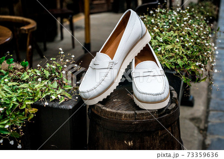 White leather moccasins. Photo on the street next to the flowers. Trendy white loafers. Fashionable women's leather shoes. White leather moccasins. Photo on the street next to the flowers. Trendy white loafers. Fashionable women's leather shoes. 73359636