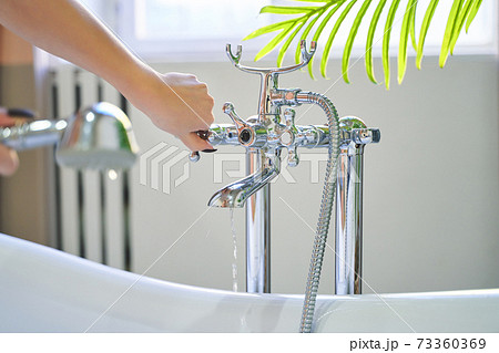 Water pours out of the shower on the girl's hands. On a blue background. Woman checks the temperature of the water in the background of the bathroom 73360369