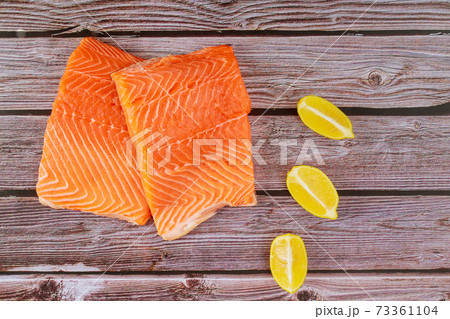 Delicious fish raw fillet salmon with lemon slices on wooden board Delicious fish raw fillet salmon with lemon slices on wooden board 73361104