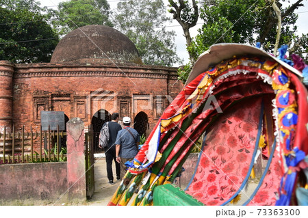 バングラデシュのダッカのショナルガオ　歴史的なゴアルディ・モスジットと停車中のリキシャと観光する男性 73363300