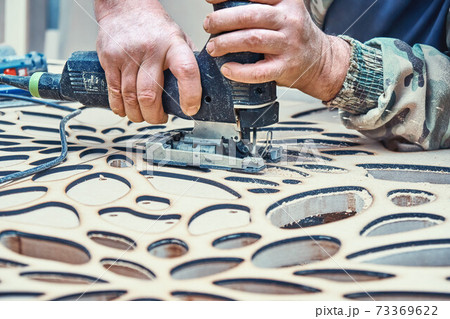 Decorative partition wall with floral pattern. Carpenter cuts holes in MDF using a jigsaw Decorative partition wall with floral pattern. Carpenter cuts holes in MDF using a jigsaw 73369622