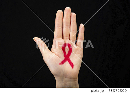 A female hand reaches up with a red awareness ribbon drawn on the palm. Black background. World AIDS day concept 73372300