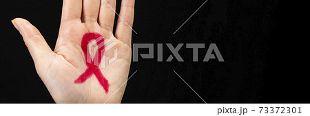 A female hand reaches up with a red awareness ribbon drawn on the palm. Black background. World AIDS day concept 73372301