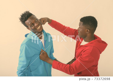 Studio shot of young black African man punching happy slim black African man smiling against white 73372698