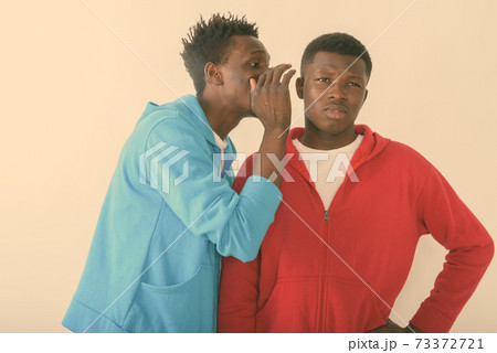 Studio shot of young slim black African man whispering to young black African man while thinking Studio shot of young slim black African man whispering to young black African man while thinking 73372721