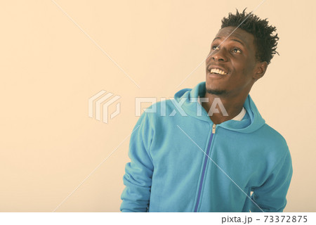 Close up of young happy black African man smiling while thinking and looking up against white 73372875