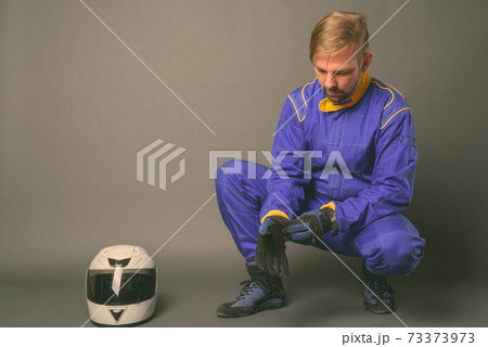 Blond bearded man motorcyclist with goatee in full gear against gray background 73373973