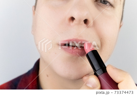 Close-up of a man painting his lips. The concept of protecting the rights of the LGBT community, a clear manifestation of homosexuality and the manifestation of female qualities in men. Close-up of a man painting his lips. The concept of protecting the rights of the LGBT community, a clear manifestation of homosexuality and the manifestation of female qualities in men. 73374473