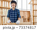 Portrait of happy Asian boy standing in carpentry workshop and holding hammer at home. 73374817